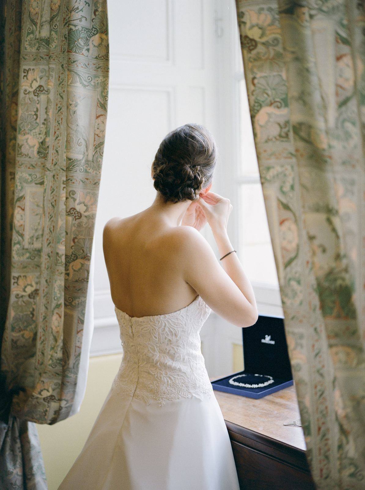 Bride putting on her earrings by the window