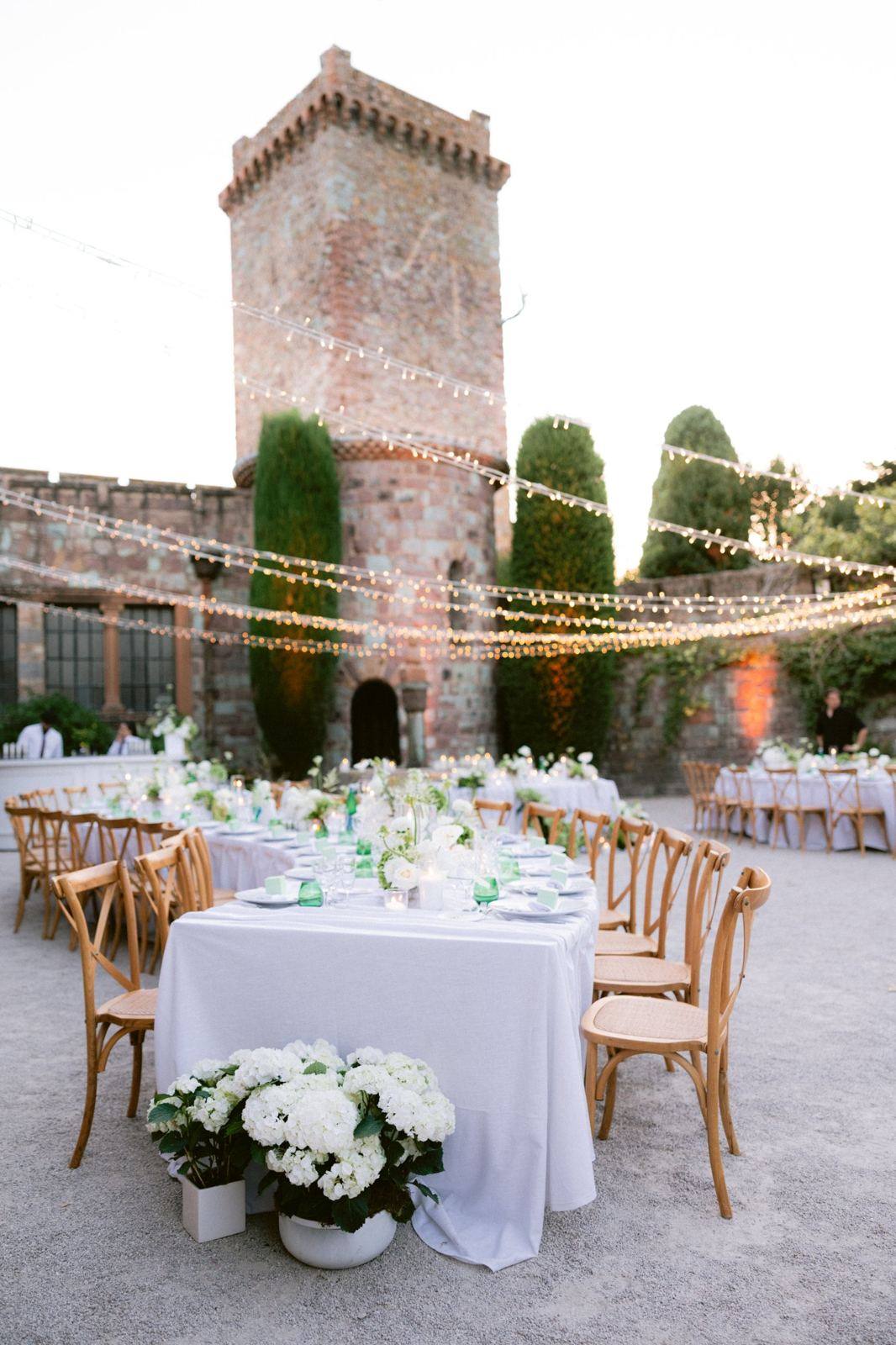 Dinner tables beneath a château tower and string lights